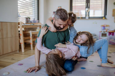 Ein fröhlicher Vater mit drei kleinen Töchtern, die zu Hause miteinander spielen. - HPIF04575