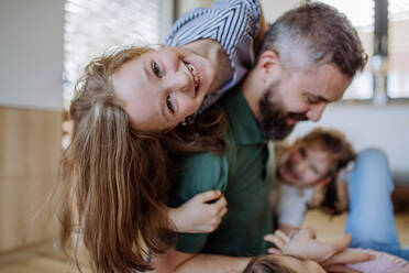 Ein fröhlicher Vater mit drei kleinen Töchtern, die zu Hause miteinander spielen. - HPIF04576