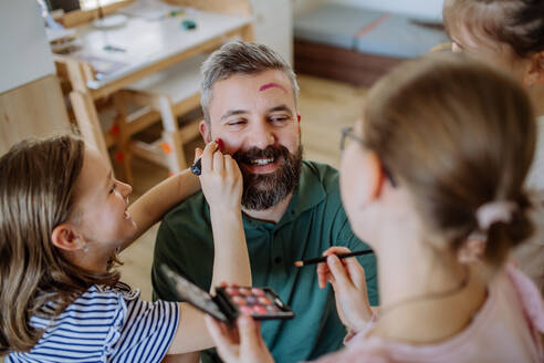 Three little girls putting on make up on their father, a fathers day with daughters at home. - HPIF04583