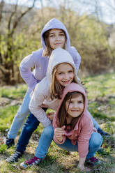 Drei kleine Schwestern, die im Frühling in der Natur gemeinsam in eine Kamera schauen. - HPIF04597