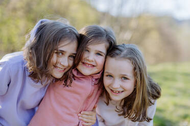 Drei kleine Schwestern, die im Frühling in der Natur gemeinsam in eine Kamera schauen. - HPIF04599