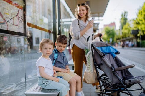 A young mother with little kids waiting on bus stop in city. - HPIF04604