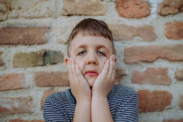 A little boy standing by brick wall and making funny faces in street summer. - HPIF04616