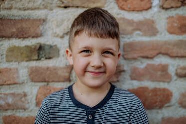 Ein kleiner Junge, der an einer Mauer steht und im Sommer auf der Straße lustige Gesichter macht. - HPIF04617