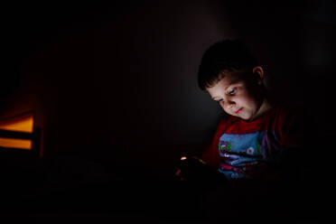 Ein süchtiger kleiner Junge spielt nachts im Bett Spiele auf seinem Handy. - HPIF04620