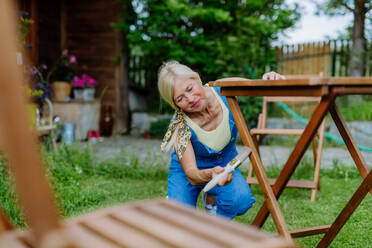 Eine ältere Frau reinigt Gartenmöbel und bereitet den Garten auf den Sommer vor - HPIF04623