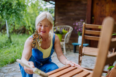 Eine ältere Frau reinigt Gartenmöbel und bereitet den Garten auf den Sommer vor - HPIF04625