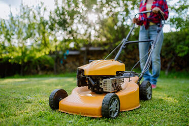 A close-up of woman mowing grass with lawn mower in the garden, garden work concept. - HPIF04643