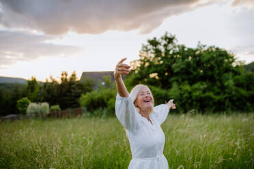 A senior woman with arms outstretched and face up at park on summer day, mental health concept. - HPIF04664