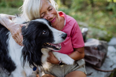 Ältere Frau ruht sich aus und streichelt ihren Hund beim Spaziergang im Wald. - HPIF04676