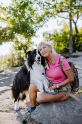 Senior woman resting and stroking her dog during walking in a forest. - HPIF04682