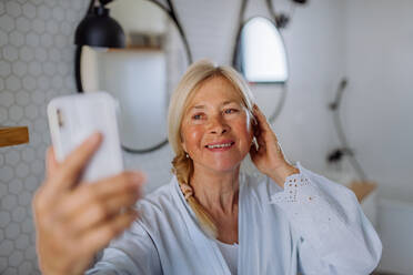 Eine fröhliche ältere Frau im Bademantel, die im Badezimmer Musik hört, Entspannungs- und Wellnesskonzept. - HPIF04727