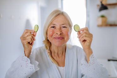 Eine schöne ältere Frau im Bademantel Anwendung Gurke Gesichtsmaske im Bad, Hautpflege-Konzept. - HPIF04729