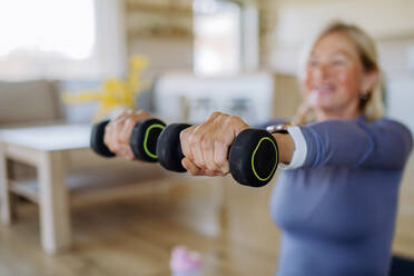 Eine fitte ältere Frau, die zu Hause mit Hanteln trainiert, Konzept für einen aktiven Lebensstil. - HPIF04736