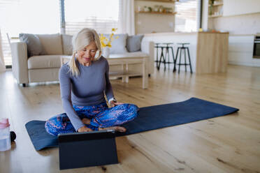 Eine fitte ältere Frau macht Dehnungsübungen zu Hause mit Tutorial auf Tablet, aktiven Lebensstil Konzept. - HPIF04739