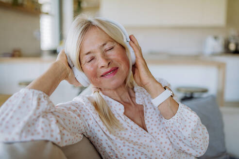 Eine ältere Frau mit Kopfhörern, die zu Hause Entspannungsmusik hört - HPIF04745
