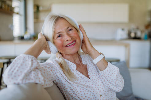 Eine ältere Frau mit Kopfhörern, die zu Hause Entspannungsmusik hört - HPIF04746