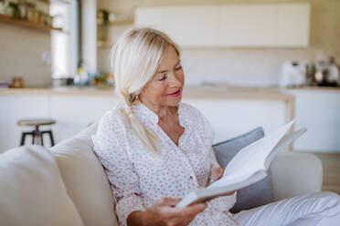 A senior woman sitting on sofa and reading book at home - HPIF04749