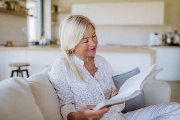Eine ältere Frau sitzt auf dem Sofa und liest ein Buch zu Hause - HPIF04749