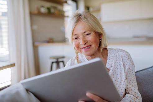 Eine ältere Frau, die zu Hause auf dem Sofa sitzt und ein Tablet benutzt - HPIF04750