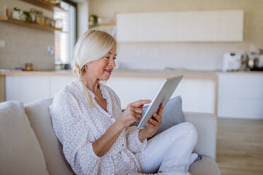 Eine ältere Frau, die zu Hause auf dem Sofa sitzt und ein Tablet benutzt - HPIF04751