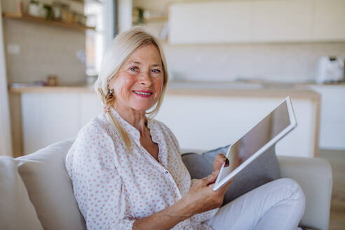 Eine ältere Frau, die zu Hause auf dem Sofa sitzt und ein Tablet benutzt - HPIF04752