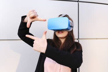 Junge Frau trägt einen Virtual-Reality-Simulator und gestikuliert vor einer Wand - ASGF03204