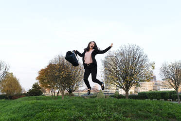 Glückliche junge Frau mit Tasche, die im Park springt - ASGF03212
