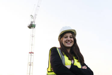 Happy female engineer with arms crossed under clear sky - ASGF03213