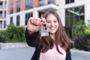 Glückliche junge Frau zeigt Hausschlüssel vor einem Gebäude - ASGF03217