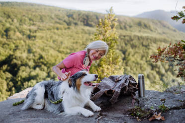 Senior woman resting and stroking her dog during walking in a forest. - HPIF04764