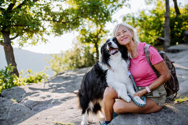 Senior woman resting and stroking her dog during walking in a forest. - HPIF04768