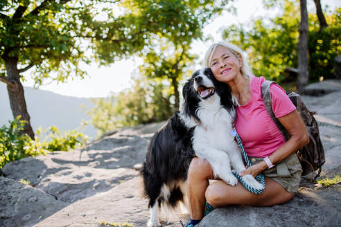 Ältere Frau ruht sich aus und streichelt ihren Hund beim Spaziergang im Wald. - HPIF04768