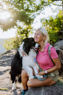 Ältere Frau ruht sich aus und streichelt ihren Hund beim Spaziergang im Wald. - HPIF04769