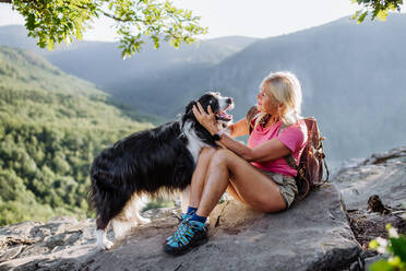 Senior woman resting and stroking her dog during walking in a forest. - HPIF04772