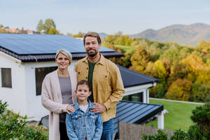 Glückliche Familie in der Nähe ihres Hauses mit Sonnenkollektoren. Alternative Energie, Ressourcenschonung und nachhaltiger Lebensstil. - HPIF04780