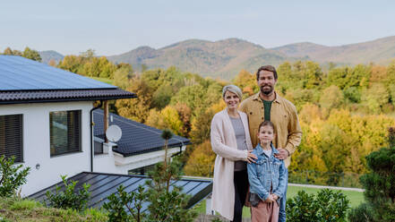 Glückliche Familie in der Nähe ihres Hauses mit Sonnenkollektoren. Alternative Energie, Ressourcenschonung und nachhaltiger Lebensstil. - HPIF04781