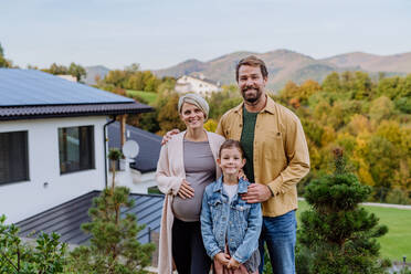 Glückliche Familie in der Nähe ihres Hauses mit Sonnenkollektoren. Alternative Energie, Ressourcenschonung und nachhaltiger Lebensstil. - HPIF04786