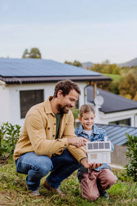 Kleines Mädchen mit ihrem Vater, der ein Papiermodell eines Hauses mit Sonnenkollektoren hält und erklärt, wie es funktioniert - alternative Energie, Ressourceneinsparung und nachhaltiger Lebensstil. - HPIF04796