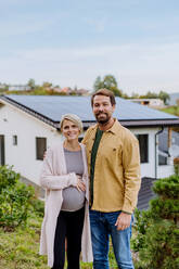 Happy man with his pregnant wife standing in front of their house with photovoltaics solar panels. - HPIF04808