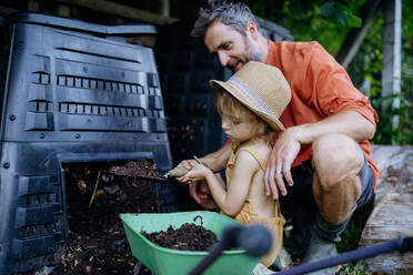 Vater mit seiner Tochter bei der Kompostierung aus einem Komposter, bäuerlicher Lebensstil. - HPIF04876
