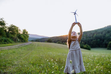 Ein kleines Mädchen steht in der Natur mit einem Modell einer Windkraftanlage. Konzept der Ökologie Zukunft und erneuerbare Ressourcen. - HPIF04898