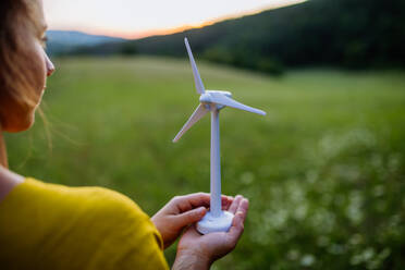 Nahaufnahme von Händen, die ein Modell eines Windturms in grüner Natur halten. Konzept der Ökologie der Zukunft und der erneuerbaren Ressourcen. - HPIF04907