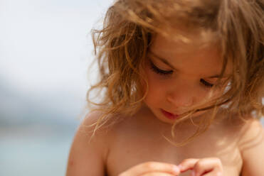 A summer outdoor close-up of little girl holding something in her hand and exploring it on holiday on beach. - HPIF04921