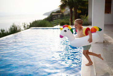 Ein glückliches Kind, das Spaß hat, wenn es mit einem aufblasbaren Ringeinhorn ins Schwimmbad springt. Sommerliche Wasseraktivitäten für Kinder. - HPIF04923