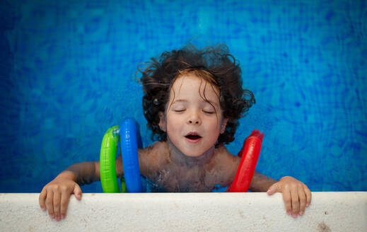 Eine Draufsicht auf ein glückliches Kind, das aufblasbare Armbänder trägt und im Schwimmbad schwimmen lernt. Sommerferienkonzept. - HPIF04924