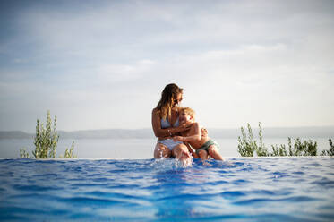 Eine glückliche Familie im Pool, Spaß haben, Mutter mit kleinem Sohn sitzen auf dem Rand des Pools und umarmt. Sommerferien Urlaub Konzept. - HPIF04926