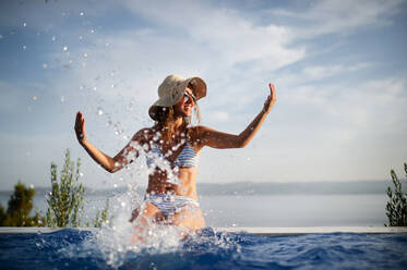 Young woman wearing hat swimming in pool at tourist resort during sunny day  stock photo