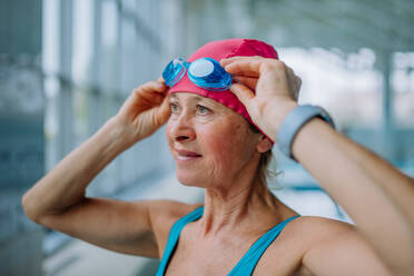 Eine Nahaufnahme einer älteren Frau, die vor dem Schwimmen im Hallenbad eine Schwimmbrille aufsetzt. - HPIF04928