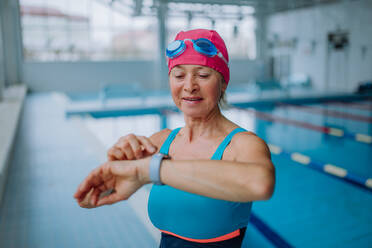 Eine ältere Frau stellt ihre Smartwatch vor dem Schwimmen im Hallenbad ein. - HPIF04930